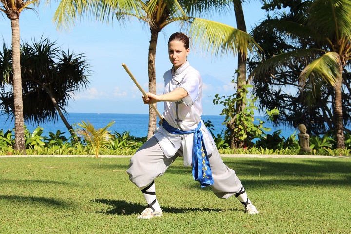 Kung Fu Kämpferin am Strand mit einem Stock.